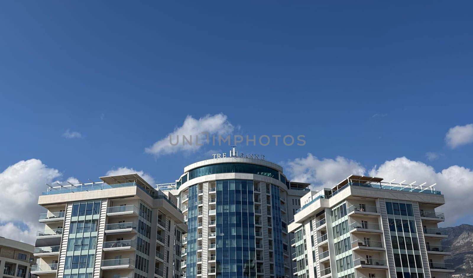 Budva,Montenegro-April 11,2025:Elegant high rise buildings of the TRE CANNE hotel with glass facades and balconies, with signage and clear sky in the background.