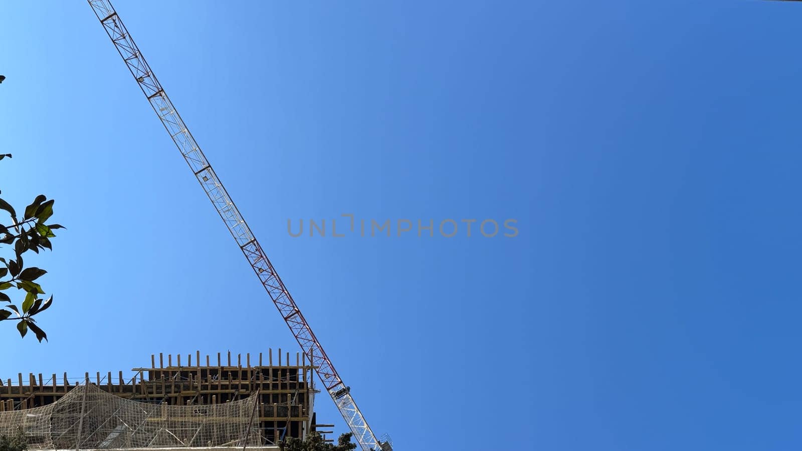 View of tall construction crane and upper part of building with scaffolding and safety net. Includes copy space. High quality photo