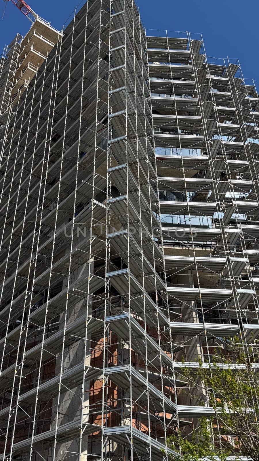 Budva,Montenegro-April 11,2025:Tall building covered in dense scaffolding under construction, viewed from below against a clear blue sky. High quality photo