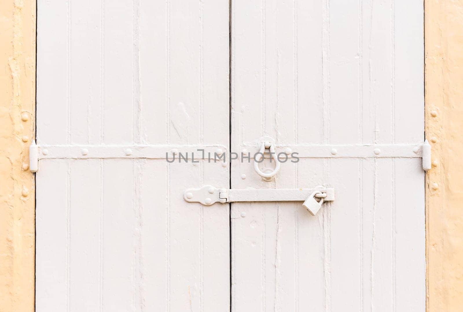 Closed vintage garage gates made of wooden palnks and an iron lock on it painted in beige and ochre colors.