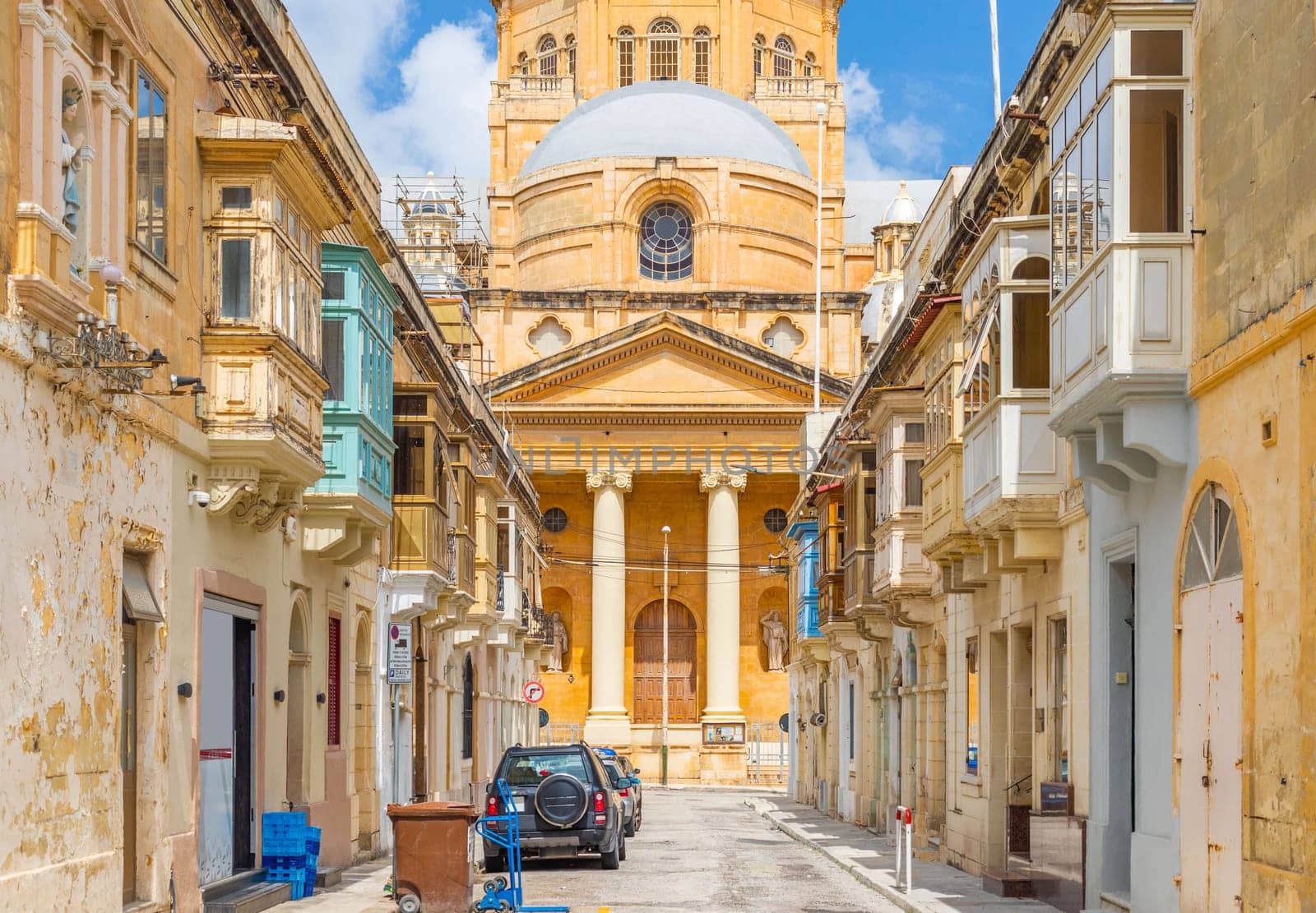 View of the Basilica of Christ the King in Paola through a narrow street with traditional Maltese houses, Tarxien, Malta.
