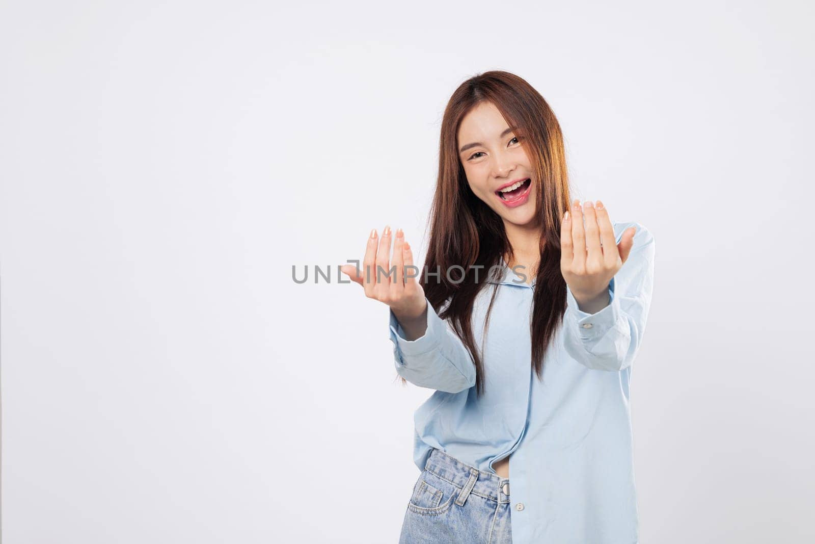 Woman uses hand gesture to beckon come here, while another woman stands with palm extended in a welcoming pose, cheerful expressions isolated in white studio background.