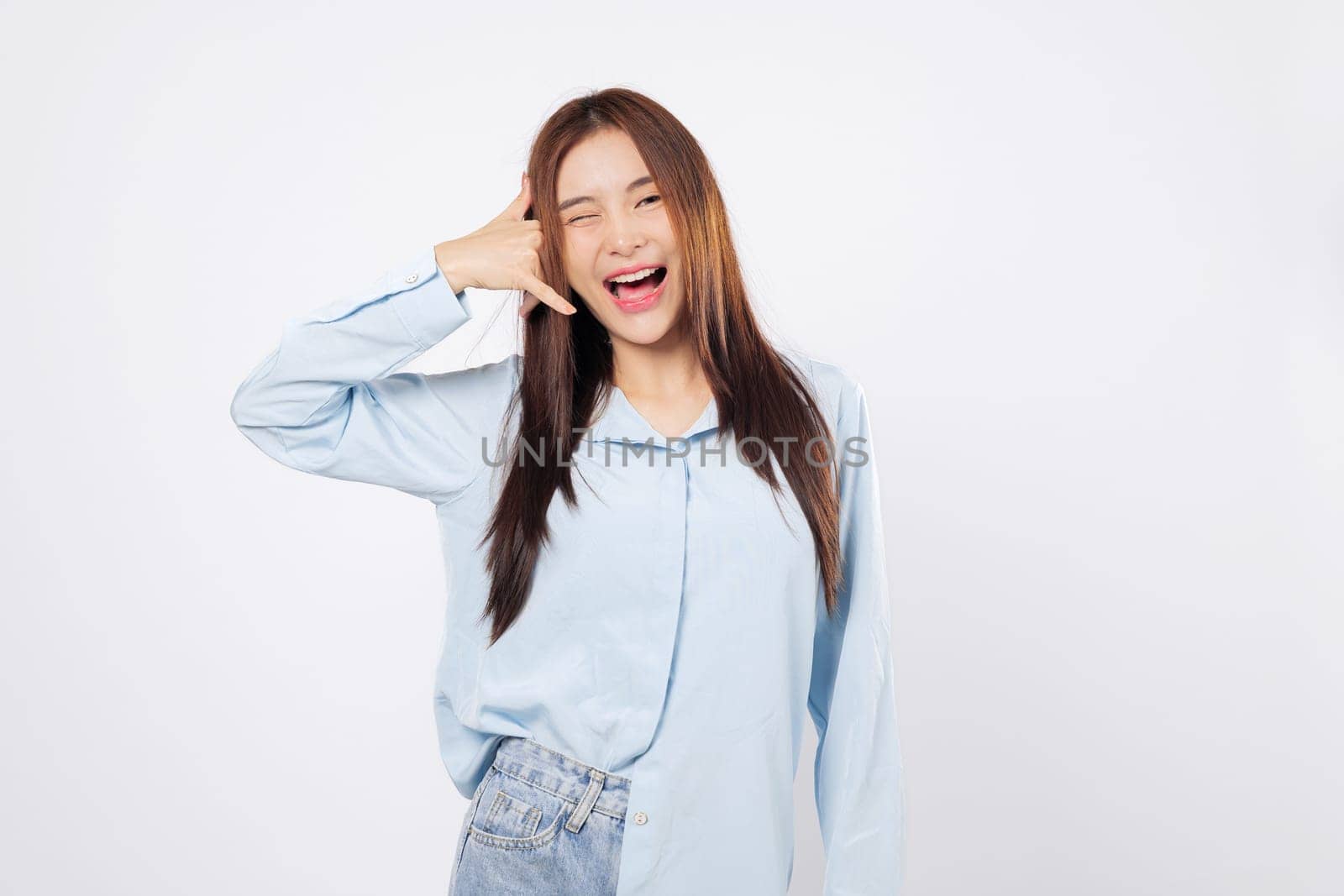 Woman making call me gesture with fingers, another woman smiles winking while mimicking a phone with hand near face, playful studio pose isolated on white background.