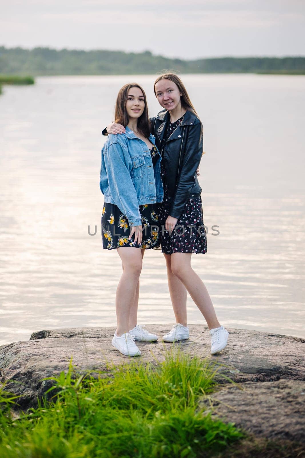Female friends embracing on lakeside boulder, sharing warm moment of connection during outdoor adventure