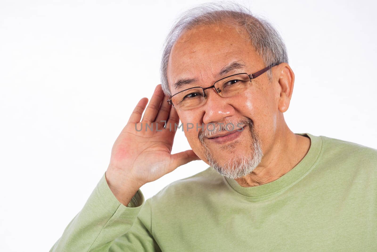 Portrait Asian old man with glasses and a beard listening to sound something, possibly engaged in conversation or trying to understand a message, hand on ear hearing a rumor isolated white background