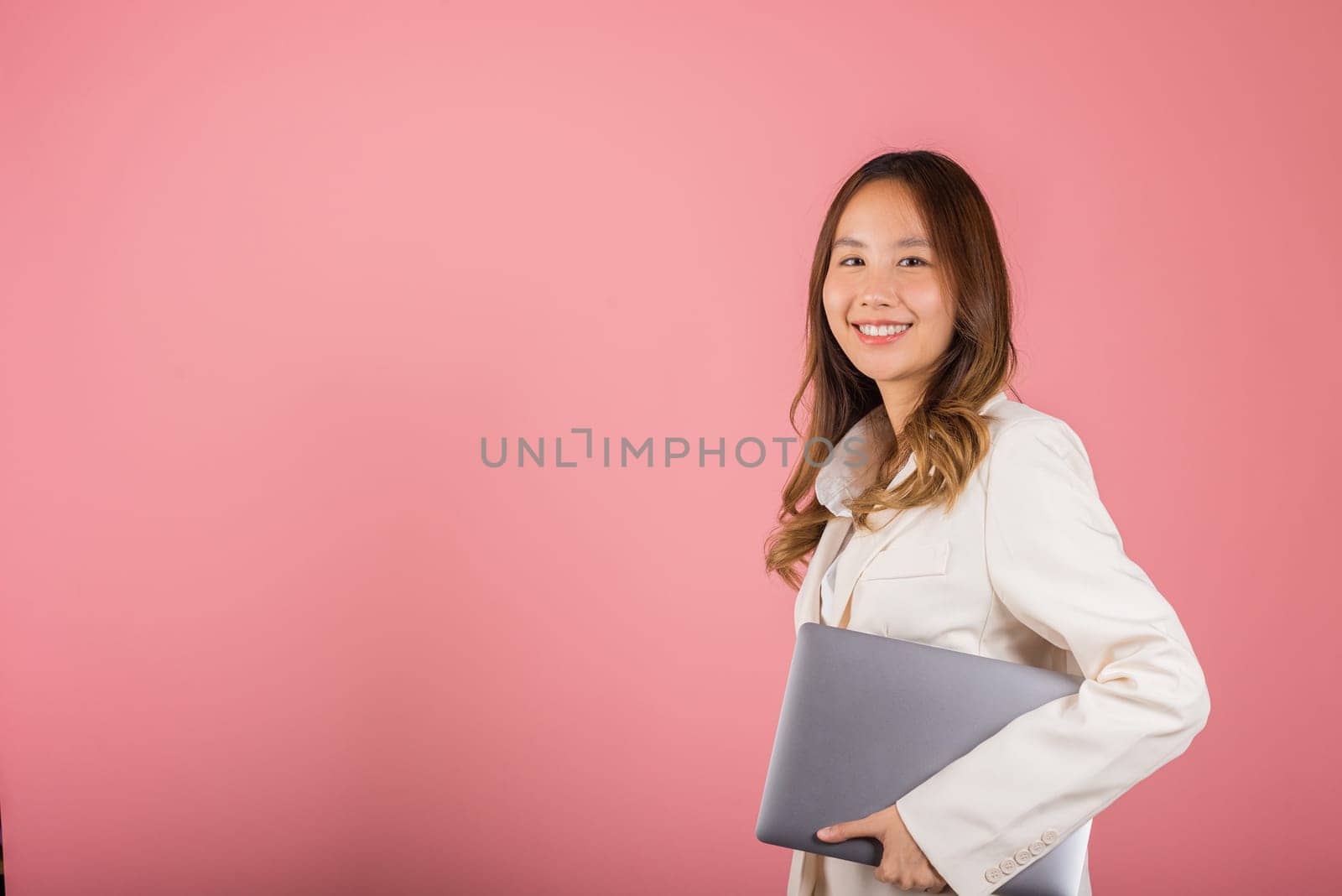 Business woman smiling confident smiling holding closed laptop, Portrait excited happy Asian young female person hugging close cover computer device studio shot isolated on pink background
