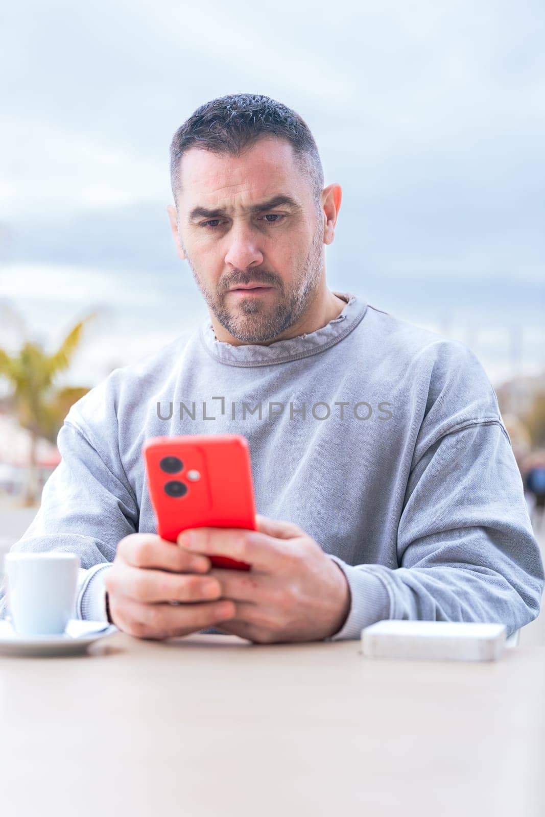serious caucasian man, serious man looking at her mobile smart phone, typing a message on the terrace of an outdoor cafe. Addiction to social networks. App, device technology concept.vertical
