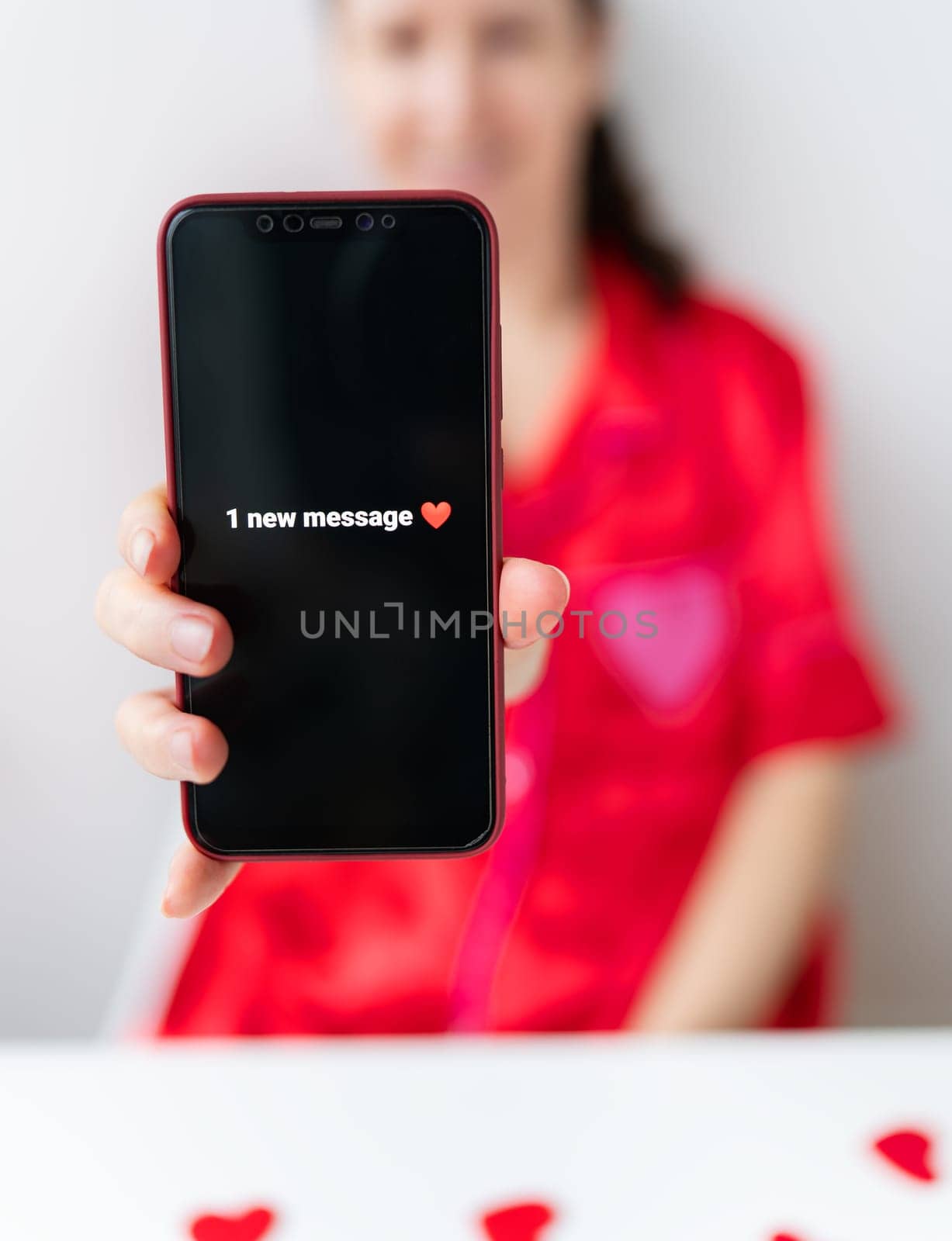 A girl holds a smartphone with a notification that says 1 new message. The focus is on the phone, and the girl is wearing a red shirt against a white background
