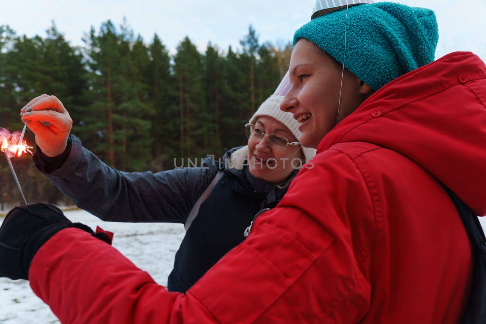 Celebrating joyfully in a snowy forest with sparklers and festive hats during a chilly winter gathering