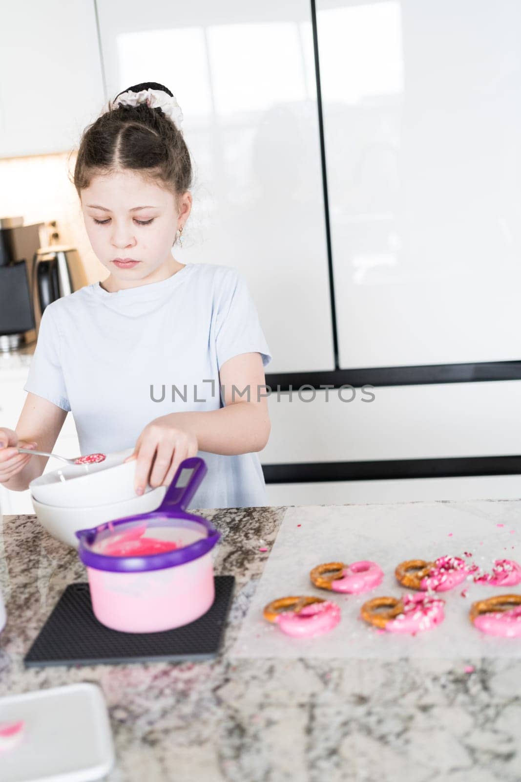 With focused attention, this budding culinary artist dips pretzels into a pot of melted chocolate, creating sweet delights in the warmth of a well-lit home kitchen.