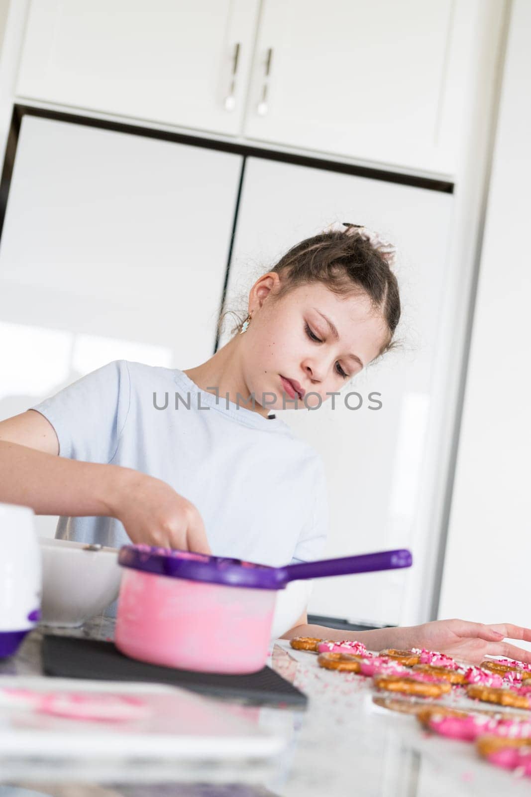 With focused attention, this budding culinary artist dips pretzels into a pot of melted chocolate, creating sweet delights in the warmth of a well-lit home kitchen.