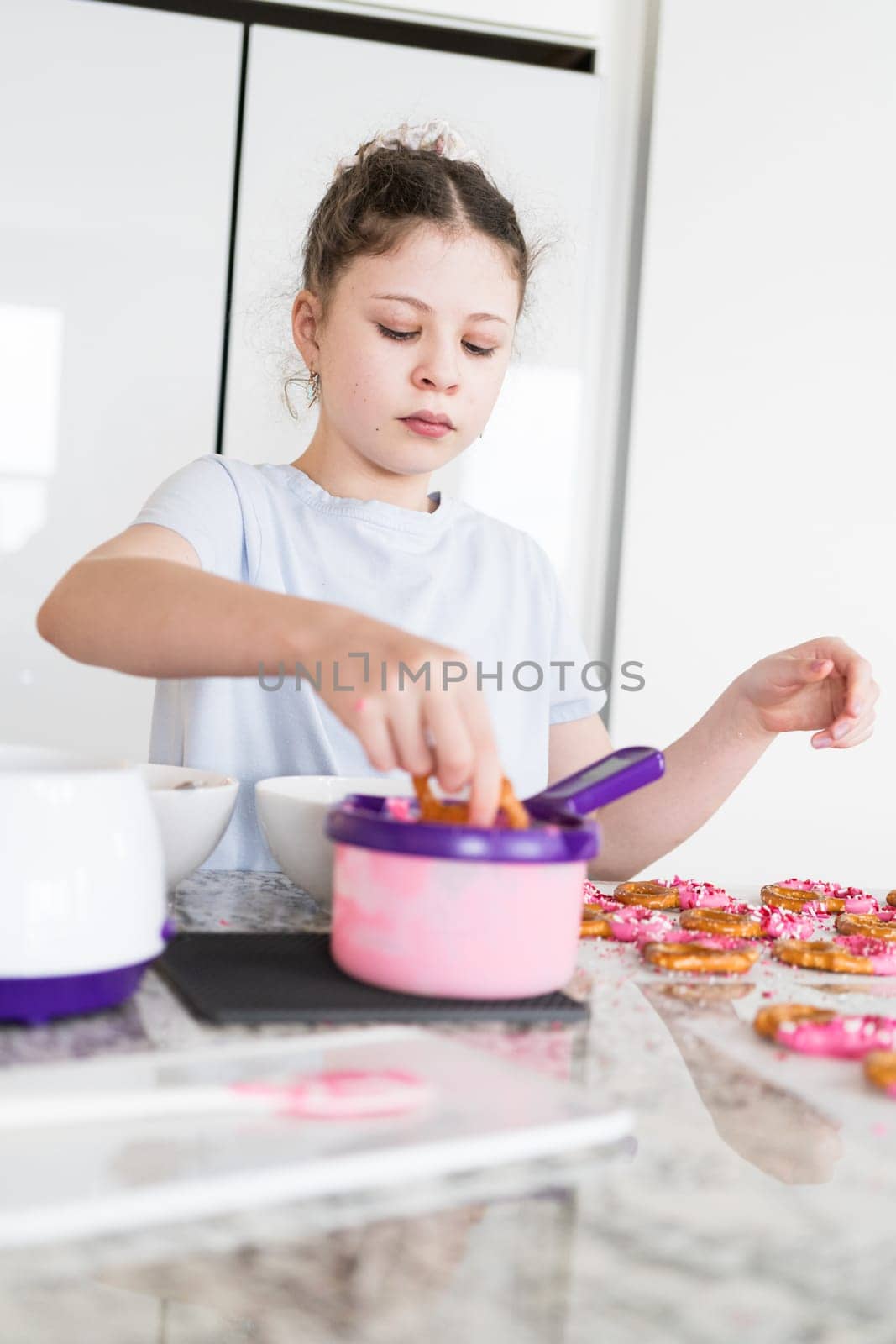 With focused attention, this budding culinary artist dips pretzels into a pot of melted chocolate, creating sweet delights in the warmth of a well-lit home kitchen.