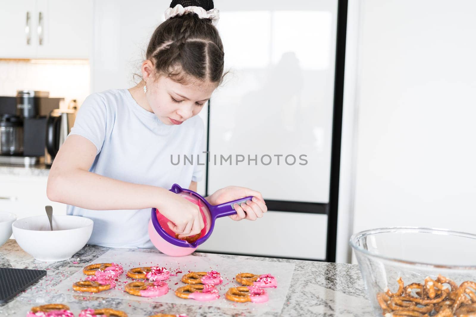 With focused attention, this budding culinary artist dips pretzels into a pot of melted chocolate, creating sweet delights in the warmth of a well-lit home kitchen.