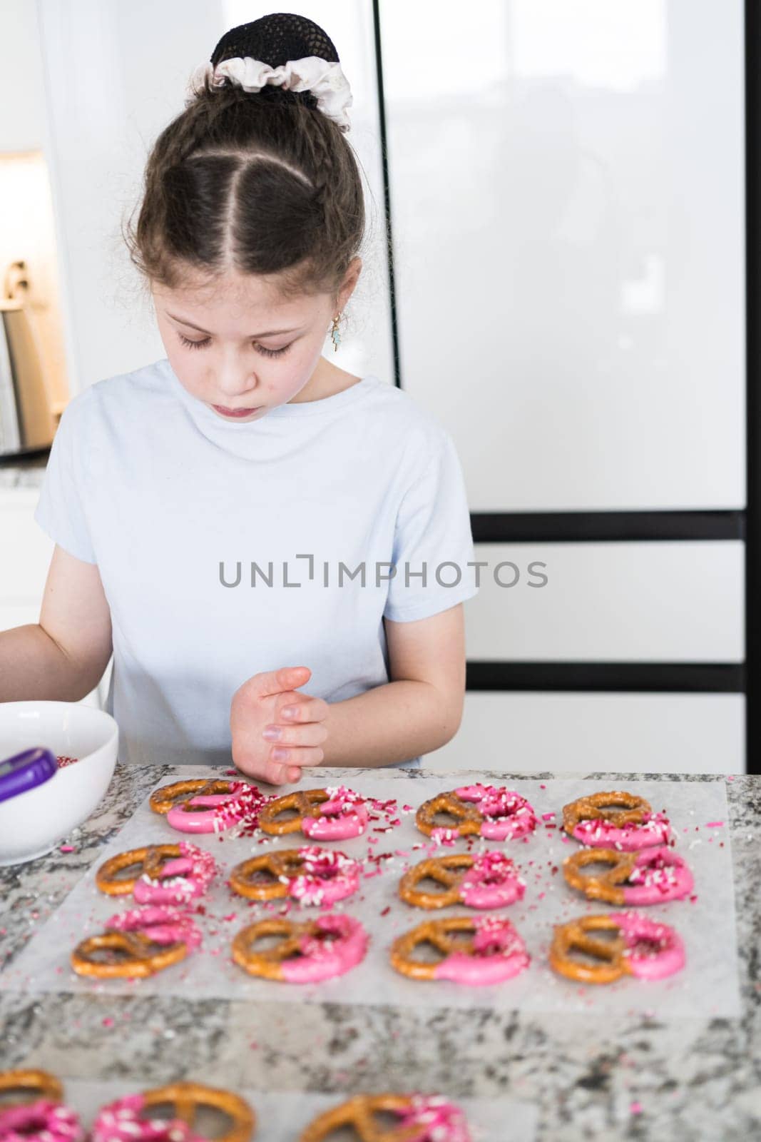 With focused attention, this budding culinary artist dips pretzels into a pot of melted chocolate, creating sweet delights in the warmth of a well-lit home kitchen.
