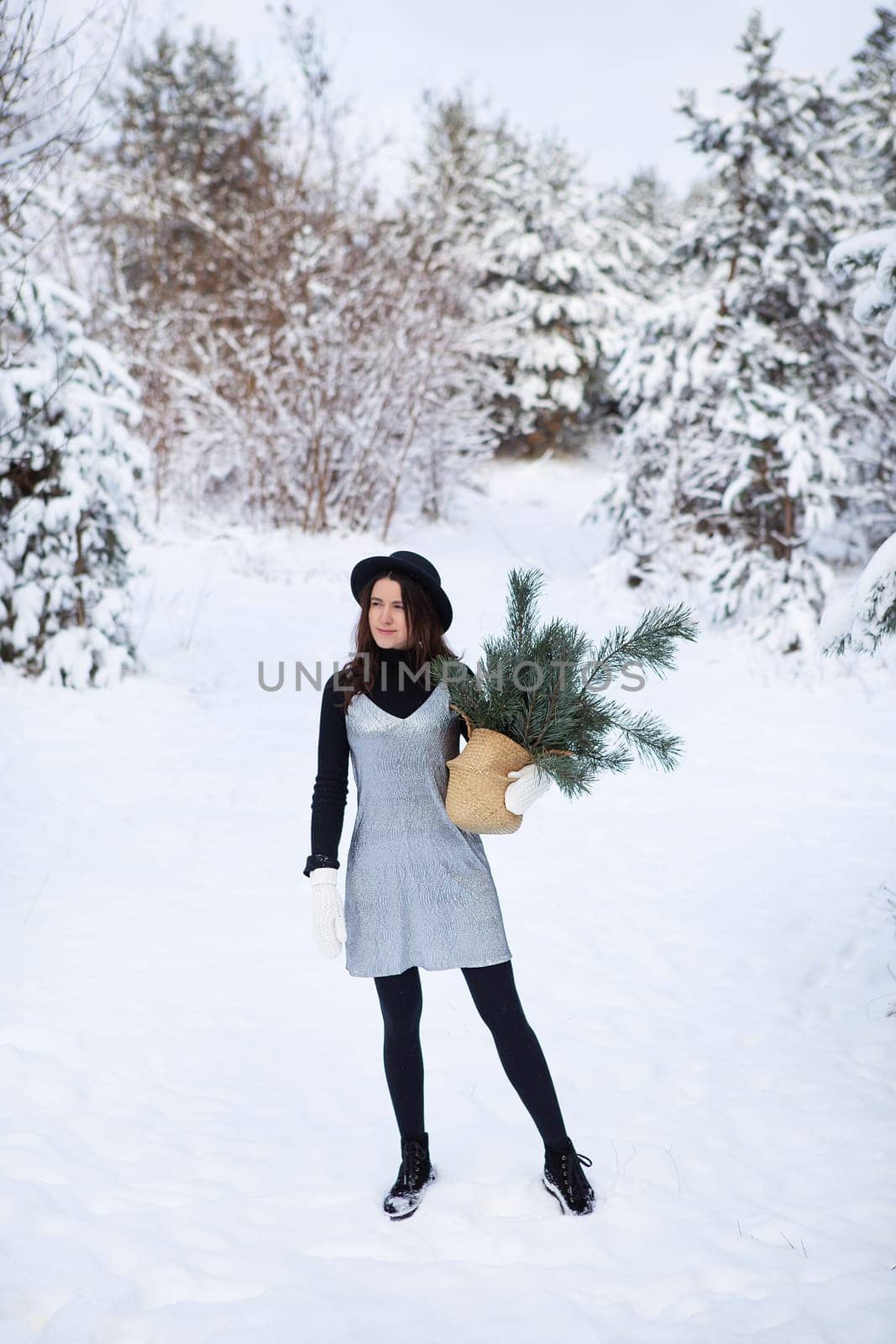 A young girl in a silvery dress and hat stands with her back in the middle of a beautiful winter forest