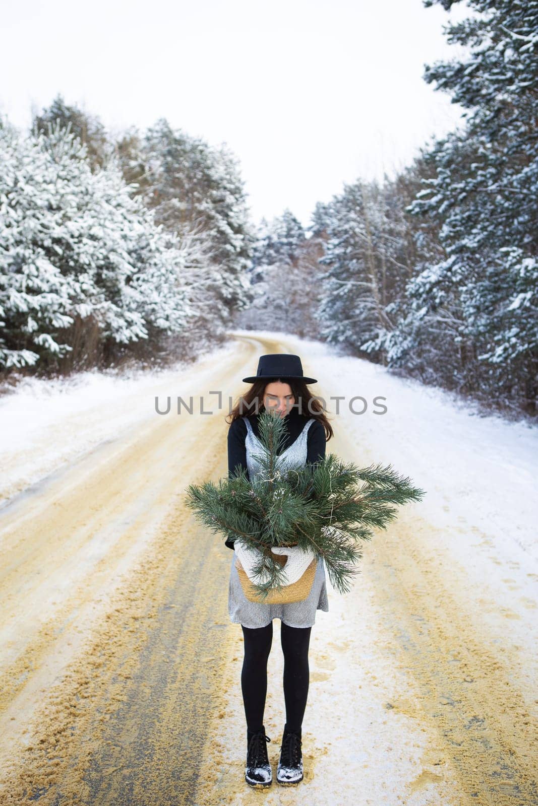 A young girl in a silver dress and hat stands with her back in the middle of a beautiful winter road in the forest