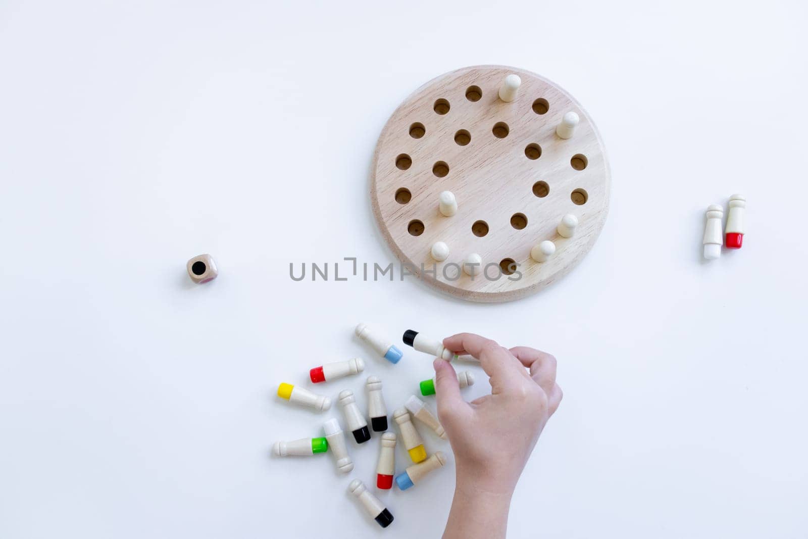 Hand playing strategy board game with wooden pegs and pegboard on white surface.