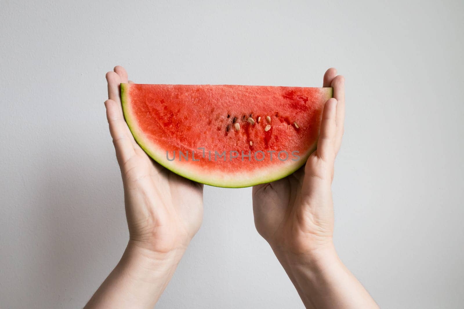 Hands holding fresh watermelon slice against white background.