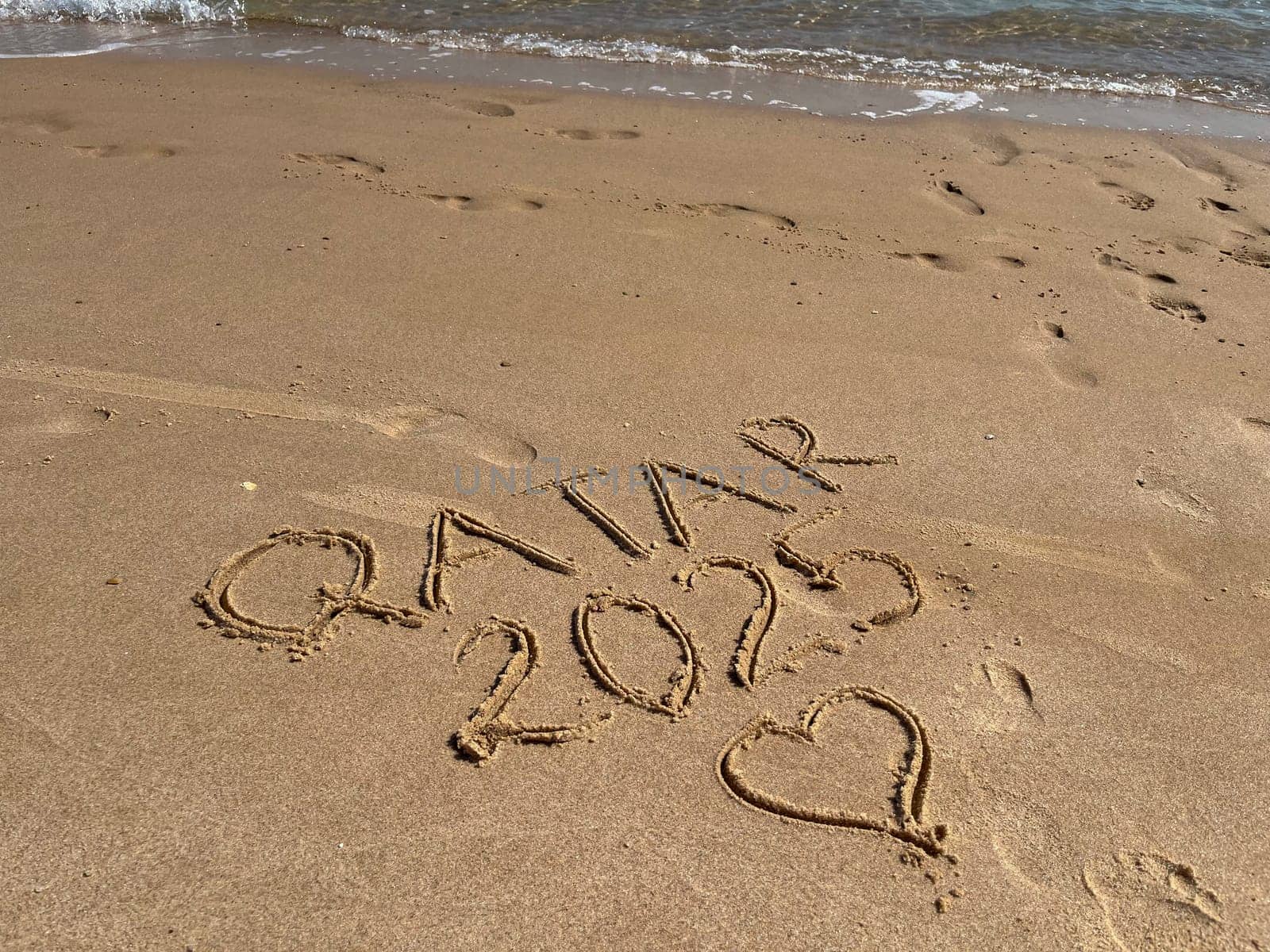 An inscription on a clean yellow sand beach in Doha, Qatar, 2025