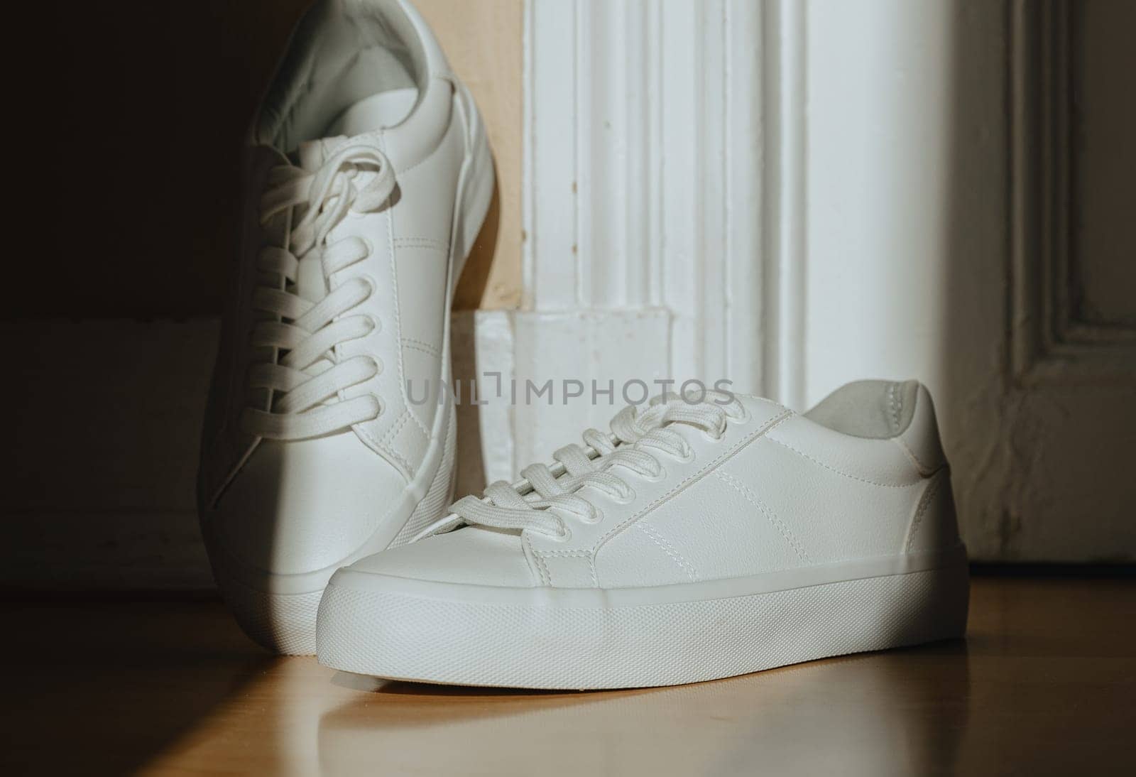 One pair of beautiful white classic sneakers with high soles and lace-ups stands on the laminate floor at the door of a home store on a sunny day, very close-up side view with depth of field. Women's shoes concept, product advertising.