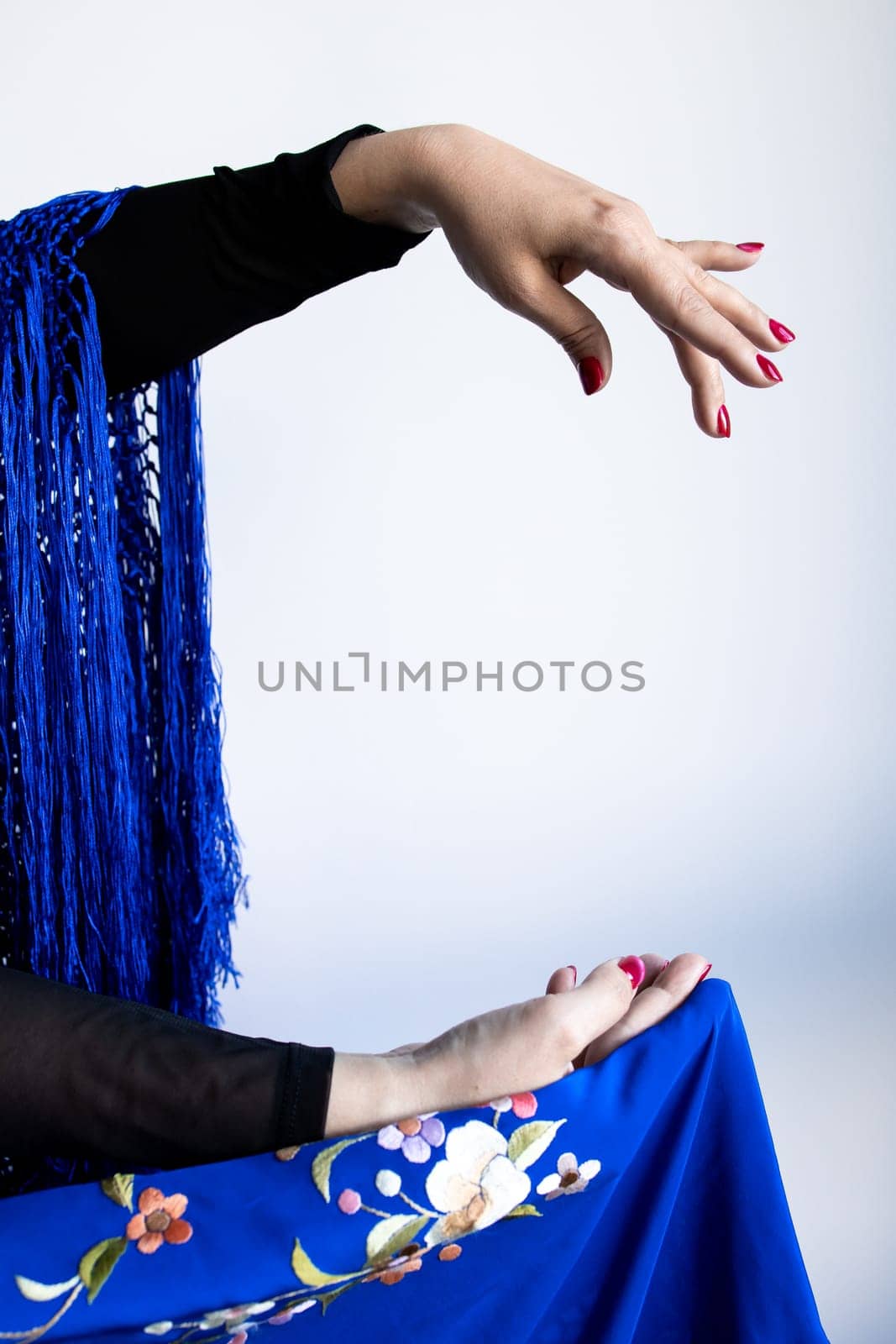 Asian female hand gesture with traditional blue embroidered shawl and red nails.