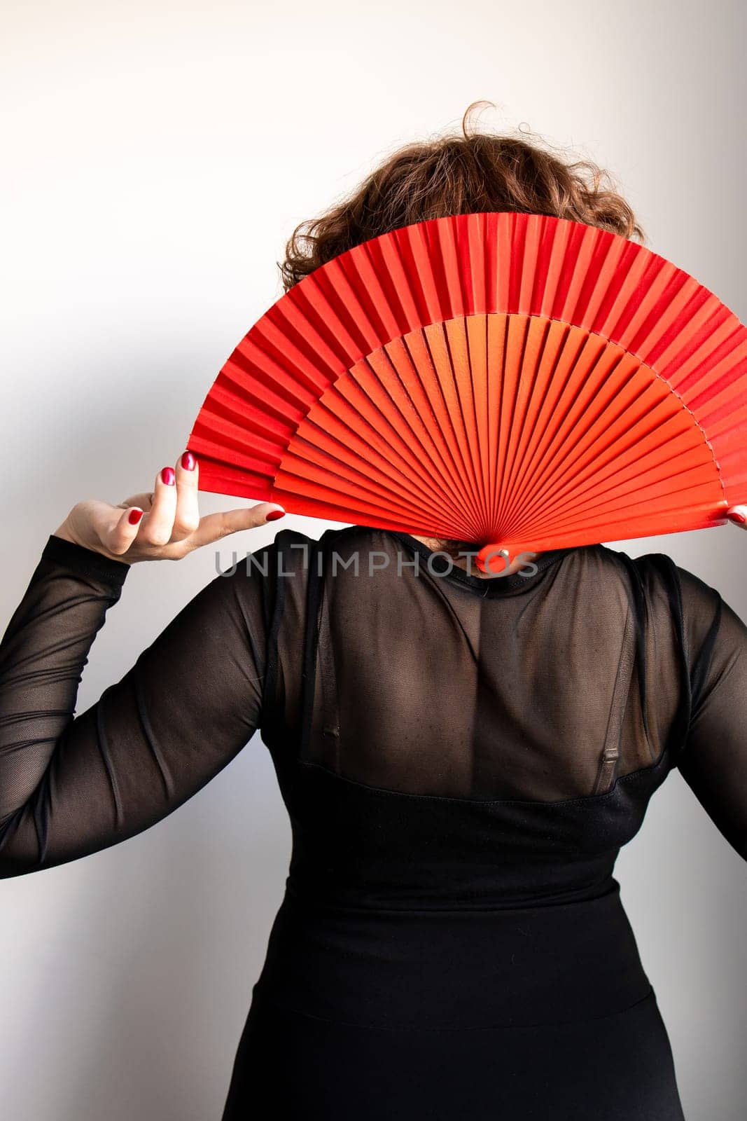Female adult with red fan and black dress viewed from behind.