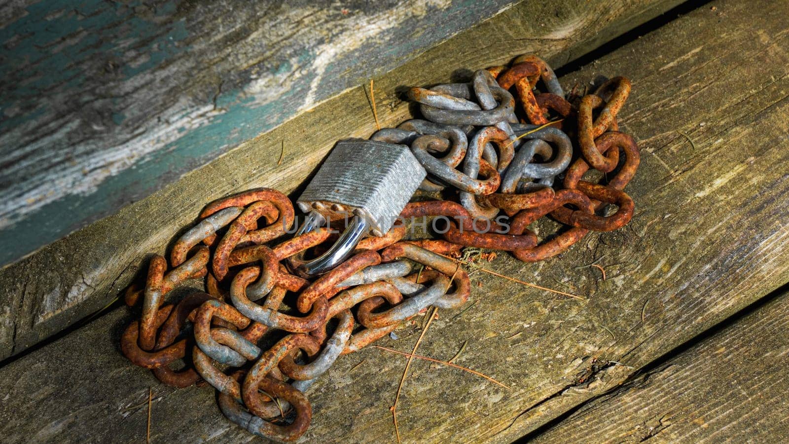 A close-up of a rusty chain and heavy padlock on a weathered wooden surface. The chain coils around the padlock, emphasizing themes of security, strength, and permanence in a rustic setting.