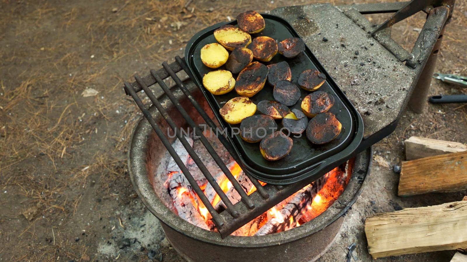 A close-up of rustic potatoes cooking on a campfire grill grate, highlighting their charred and crispy exterior while revealing the soft and fluffy interior, perfect for outdoor cooking enthusiasts.