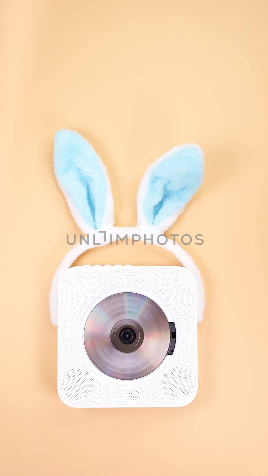 The image features a vintage white portable CD player, elegantly designed, adorned with a playful pair of blue bunny ears headband. Set against a soft peach color background, it evokes nostalgia.