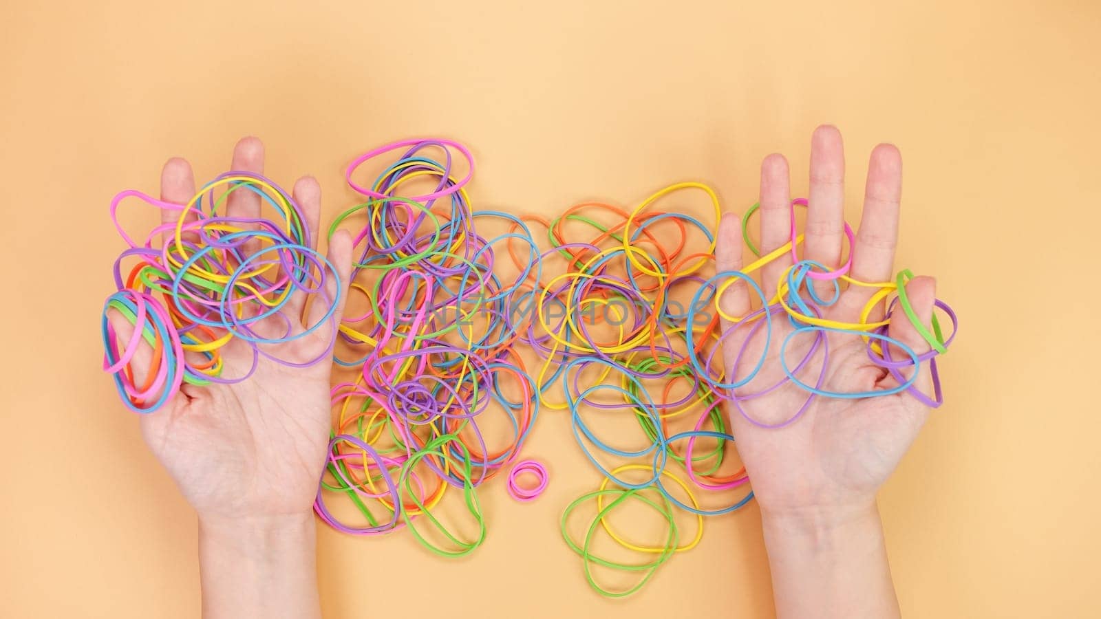 A collection of colorful rubber bands of various sizes tangles together on a soft peach background. The vibrant pink, blue, green, yellow, and orange hues create a playful and striking visual.