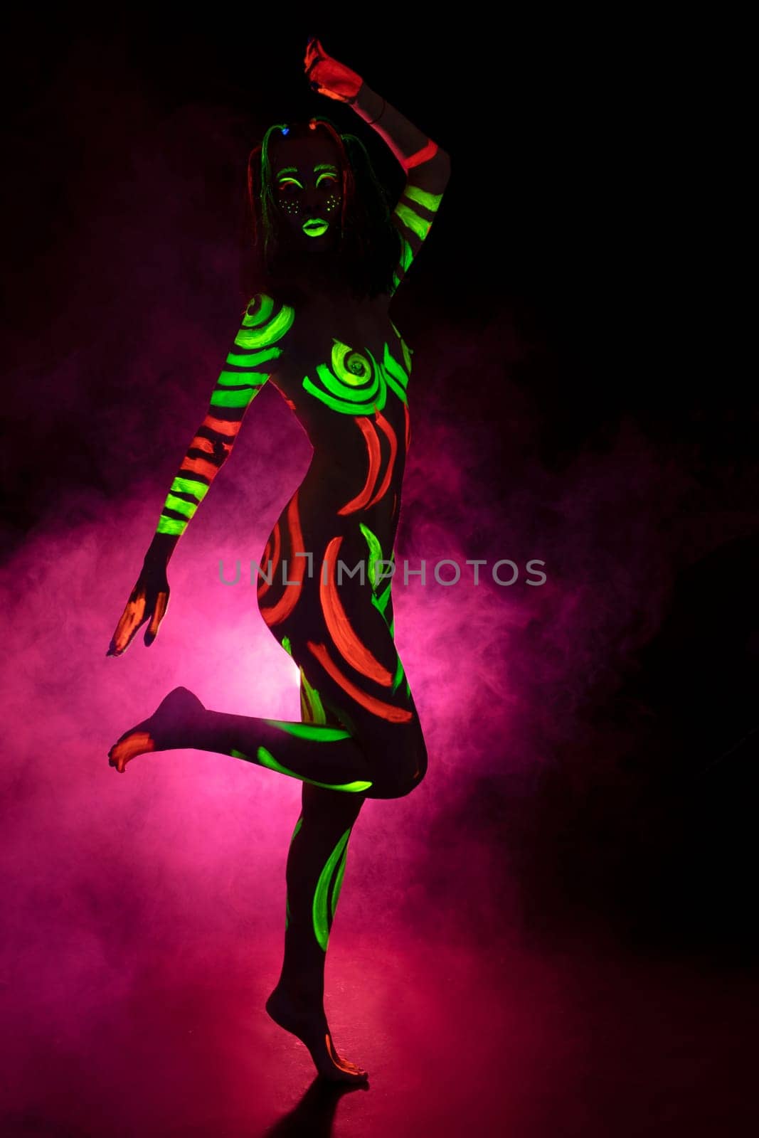 unrecognizable topless female model with bright UV paints on body and face dance in pink smoke