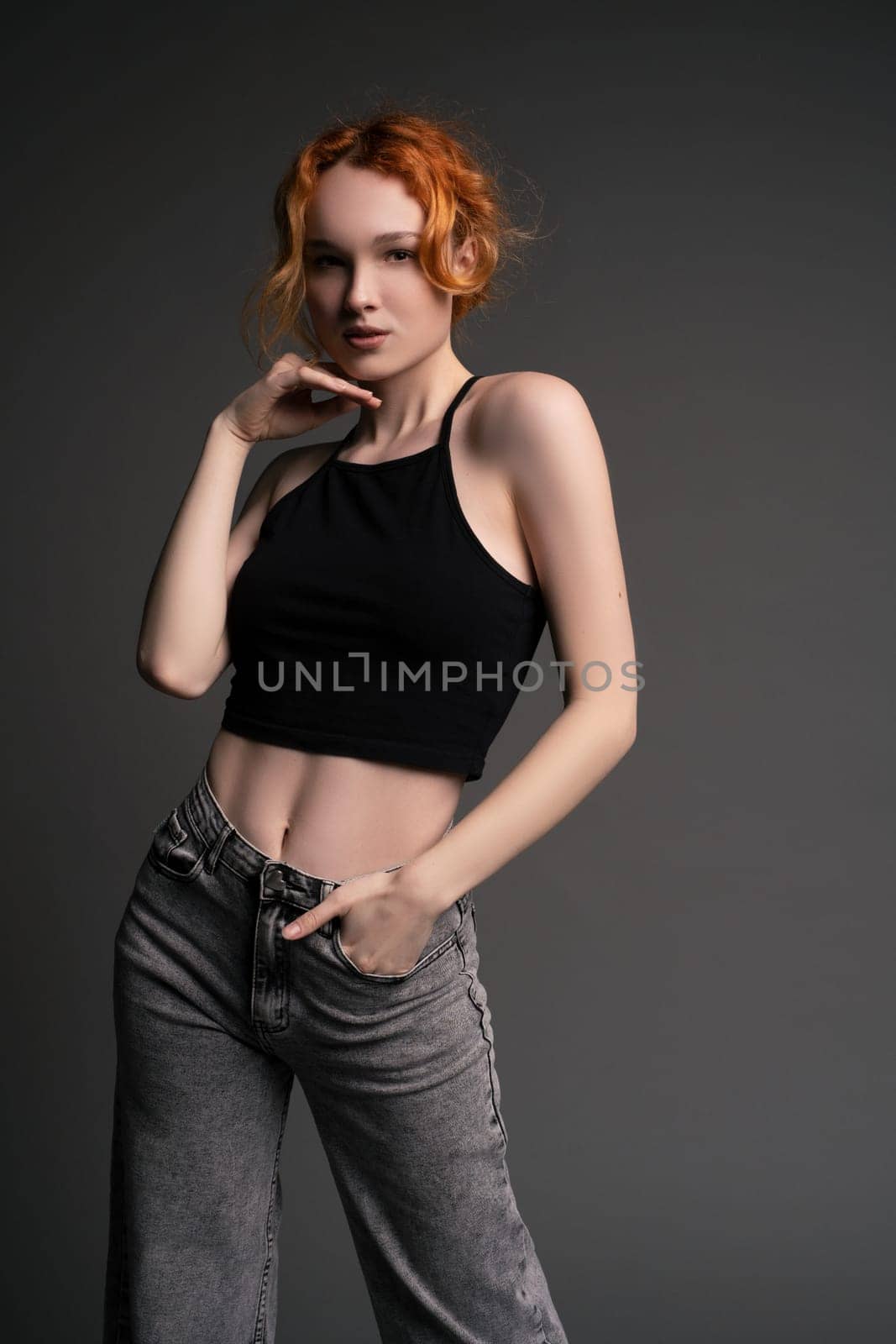 Portrait of young female model in trendy jeans and crop top with red hair touching head and looking at camera