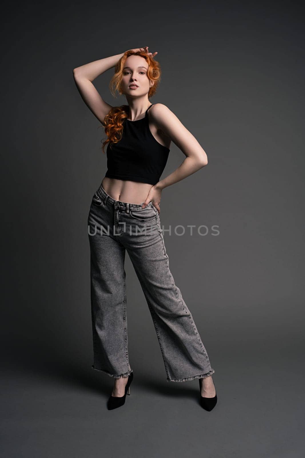 Full length of young female model in trendy jeans and crop top with red hair looking at camera during model test