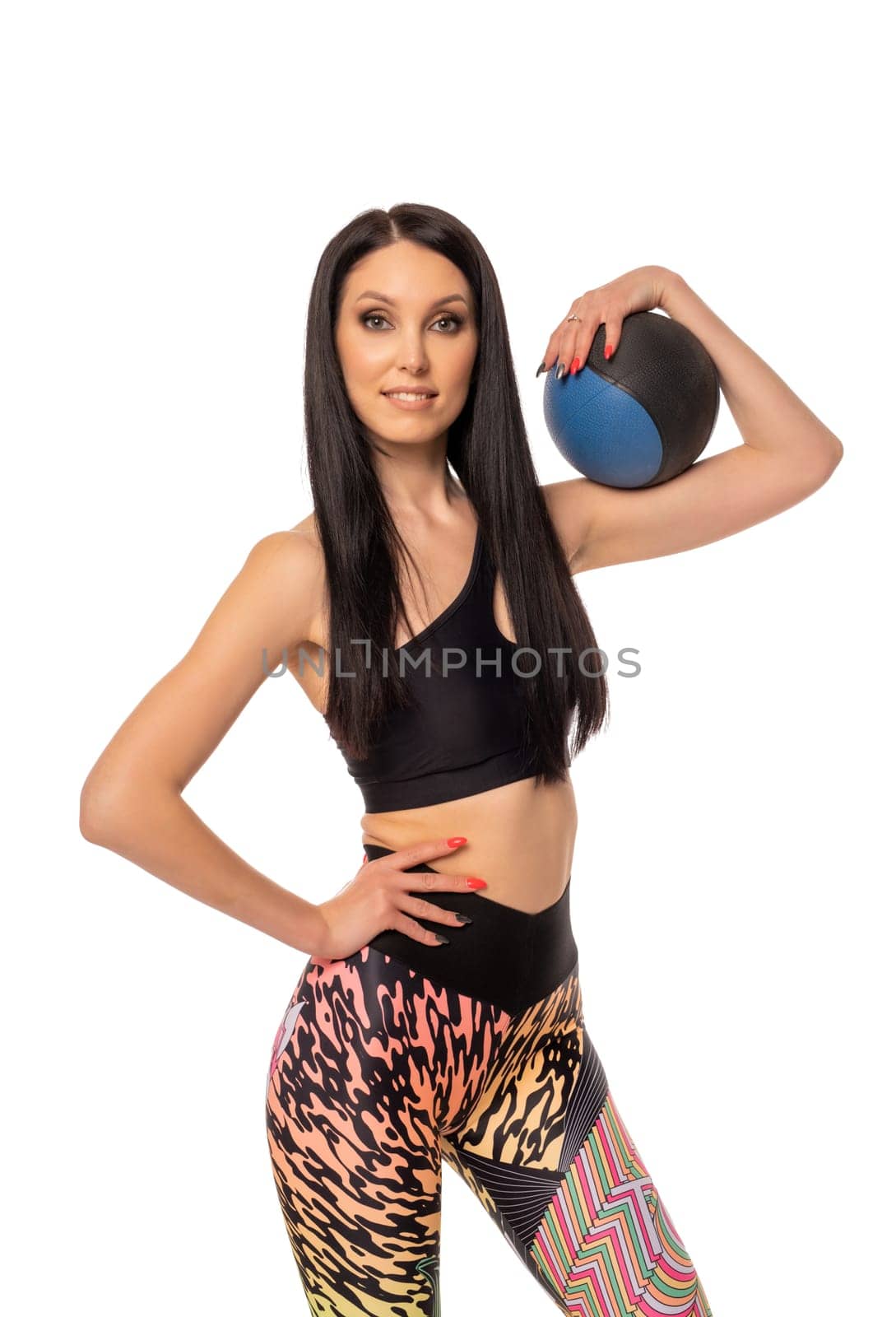 Confident young fit female athlete in sportswear lifting heavy kettlebell with hands on waist and looking at camera against white background