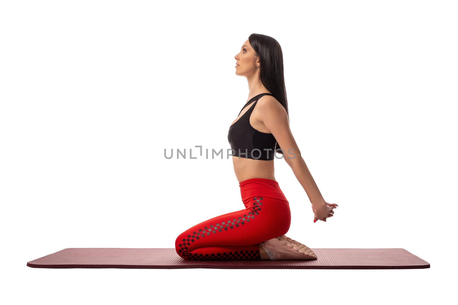 Side view of young slim female in sportswear sitting on mat and stretching legs while doing yoga in lotus pose against white background