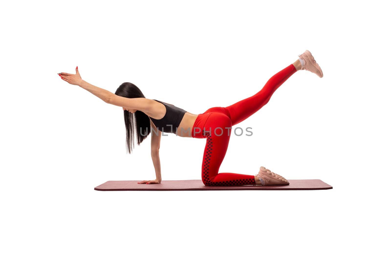 Side view of flexible female in sportswear standing on mat in pose and practicing yoga on white background