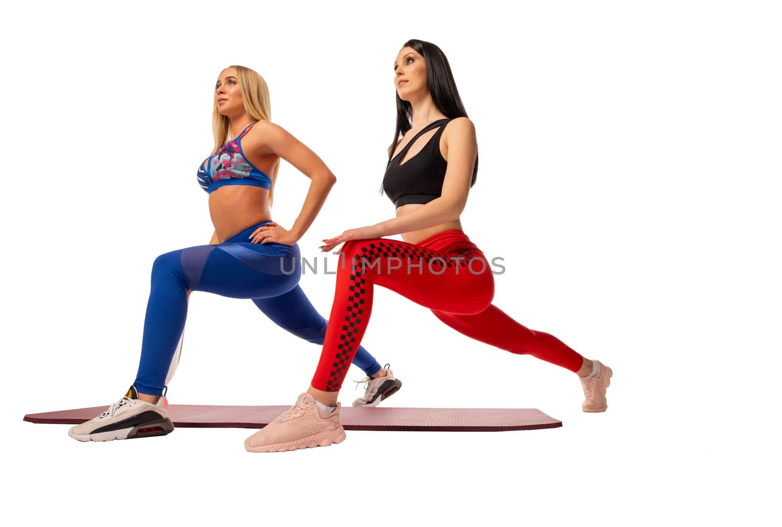 Full body of motivated young female athletes with long blond and dark hair in sportswear doing lunges exercise while training together against white background