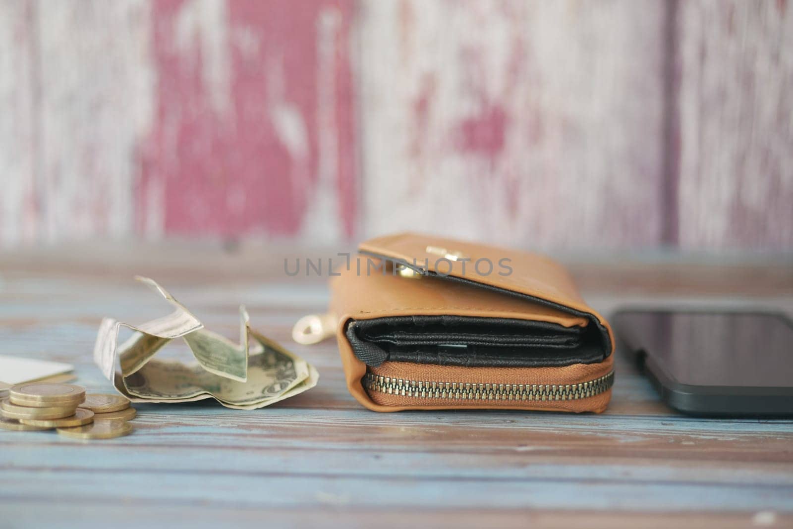 A brown wallet rests on a wooden table, surrounded by cash and coins.