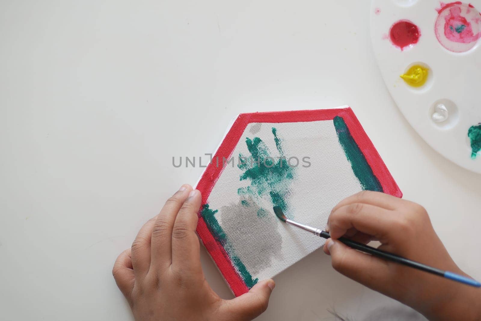 A young child paints a hexagonal canvas using vibrant colors and a brush.