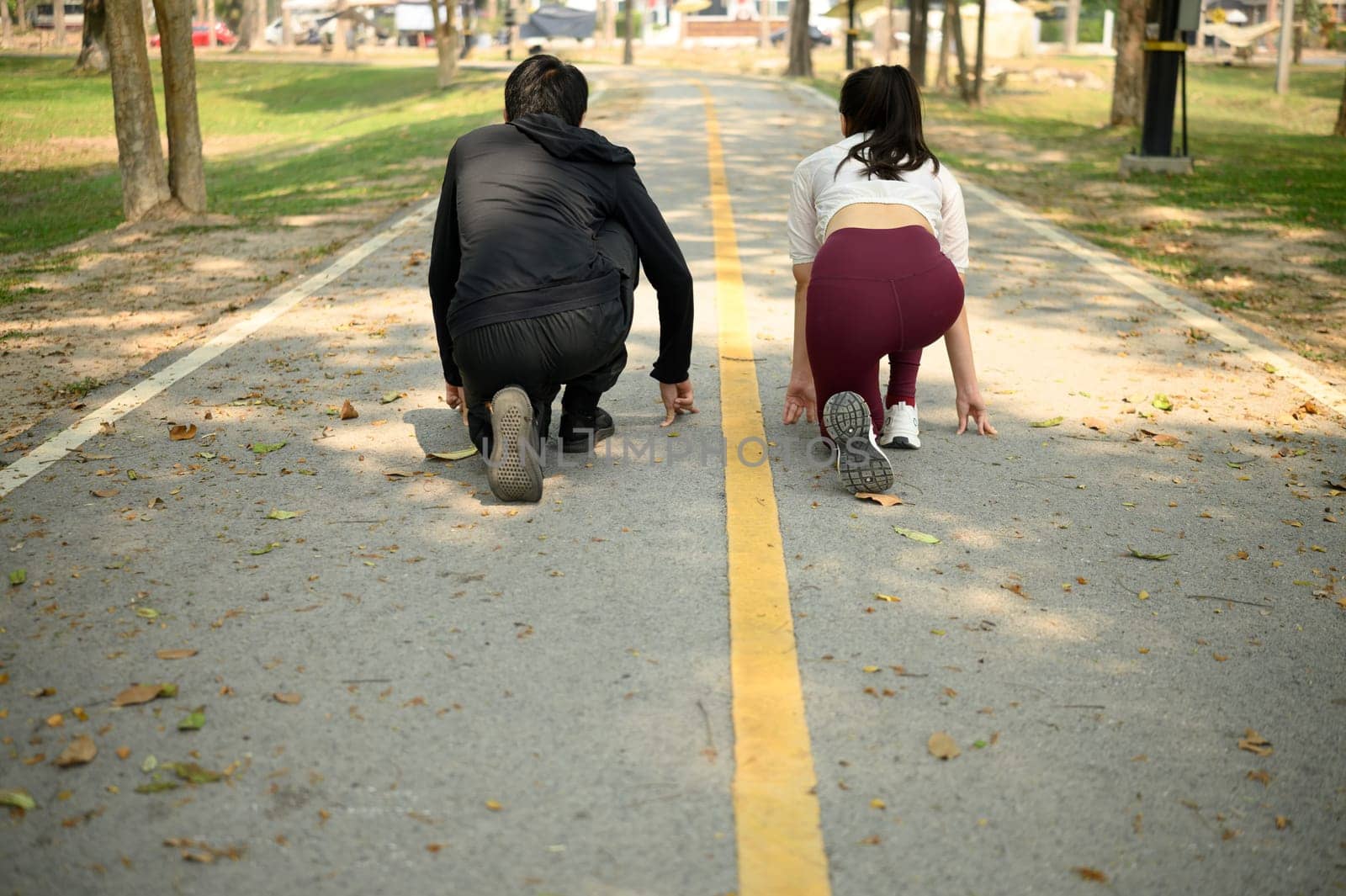 Young couple preparing to sprint in a park, crouched in starting position on a pathway.