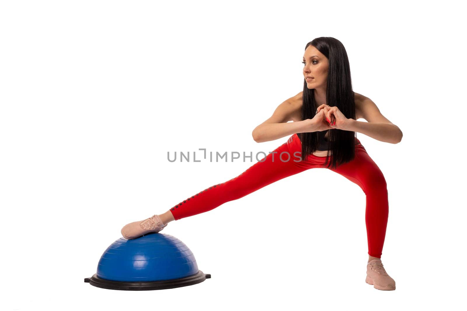 Full body side view of young slim female athlete in sportswear standing on white background in studio and looking at camera