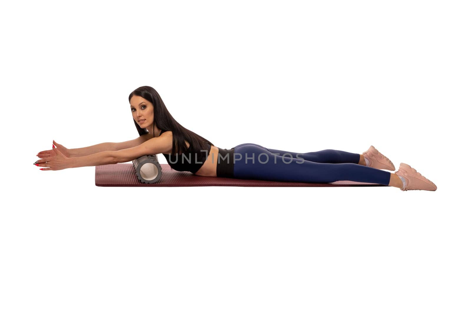 Side view of graceful young female athlete with long dark hair in activewear lying on mat with foam roll under breast while doing posture exercise