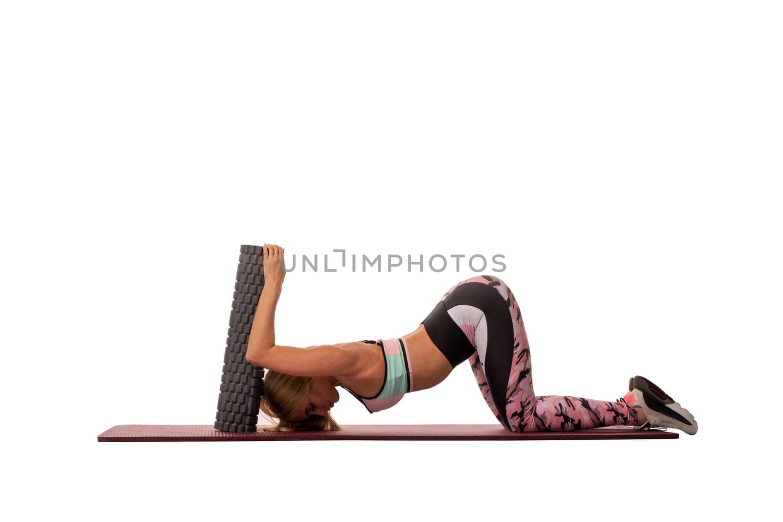 Side view of slim female in sportswear lying on mat and stretching body while practicing yoga on white background