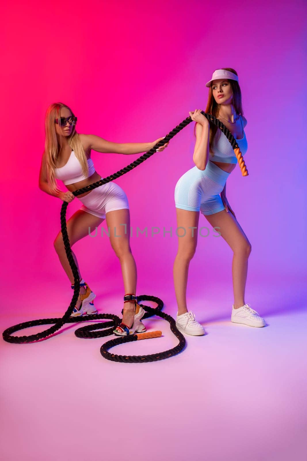 Full body side view of slim female athlete in sportswear and sneakers standing on pink background in studio