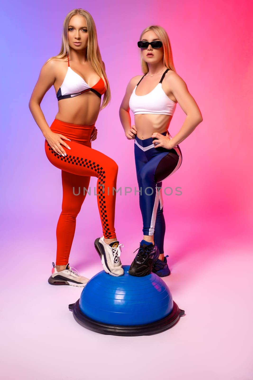 Full body of confident young female in trendy outfit and sunglasses looking at camera while standing against pink background