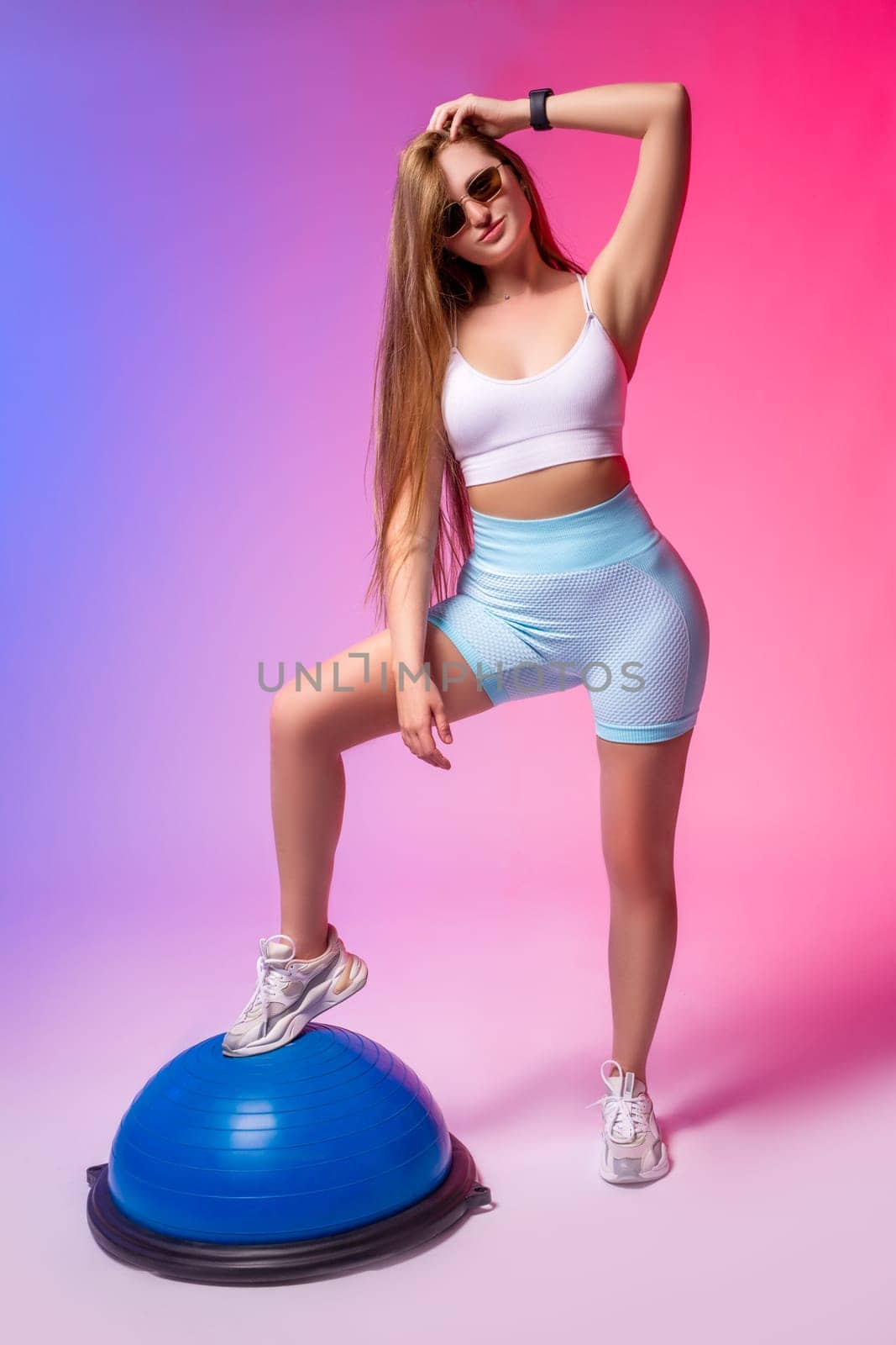 Full body of young fit female athlete in sportswear standing with raised arm and looking away against purple background