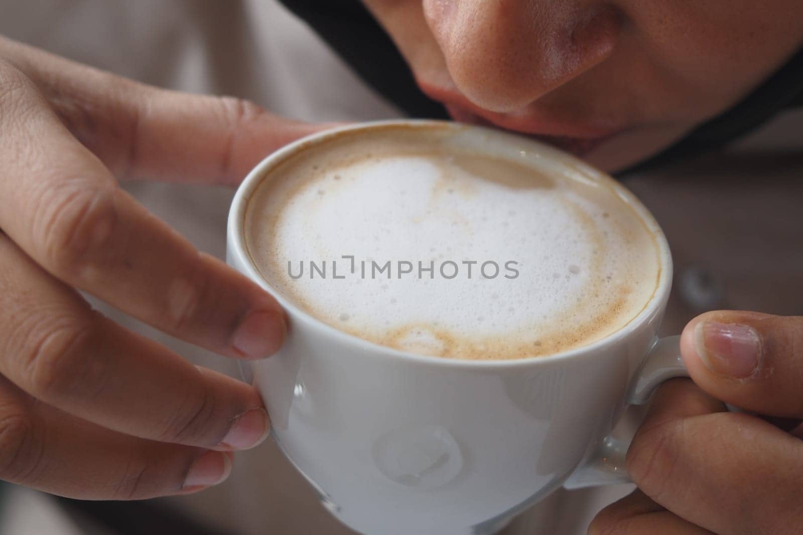 A person sips a foamy cup of coffee, savoring the moment indoors.