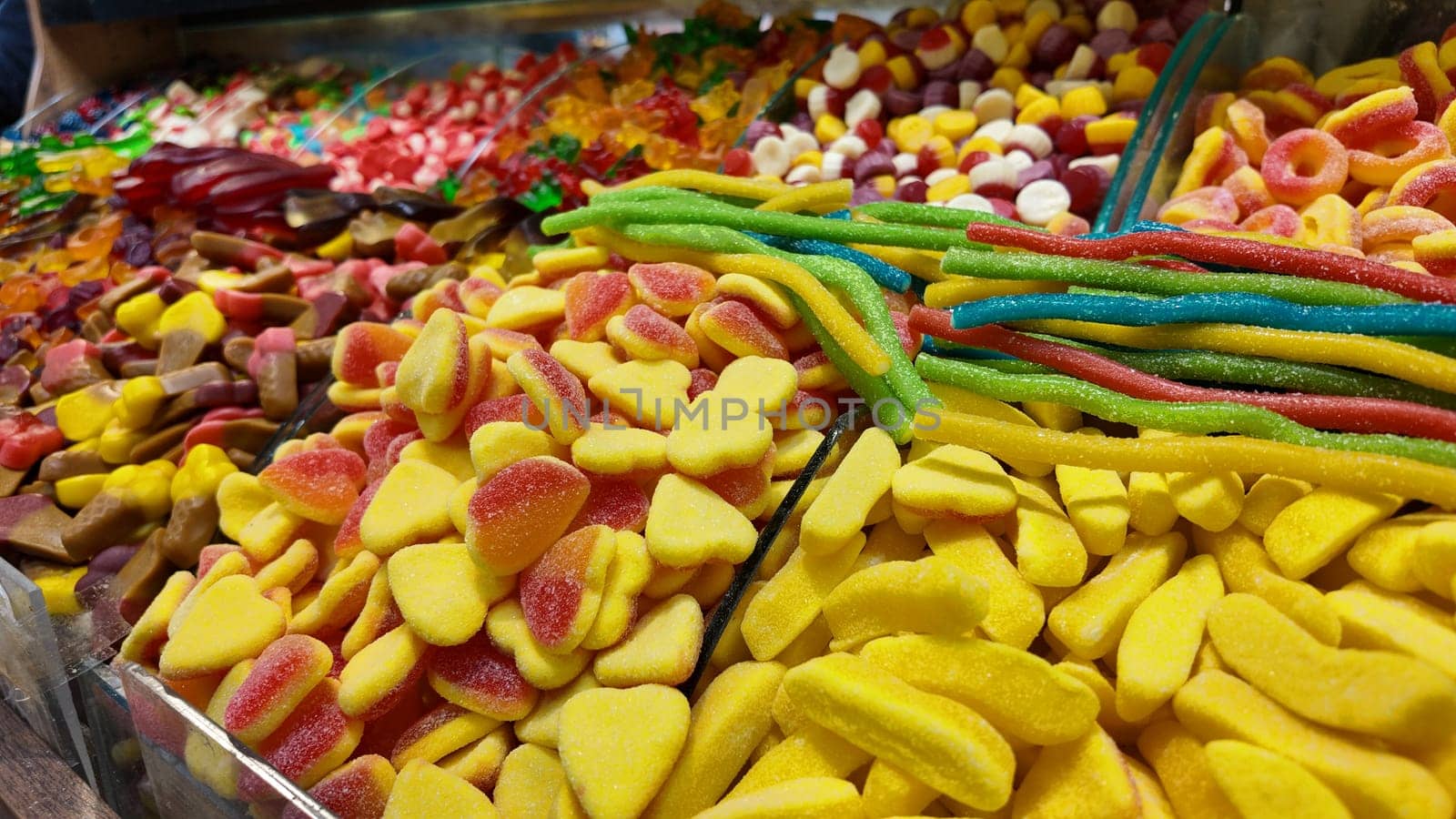 A vibrant display of various gummy candies fills a market stall.