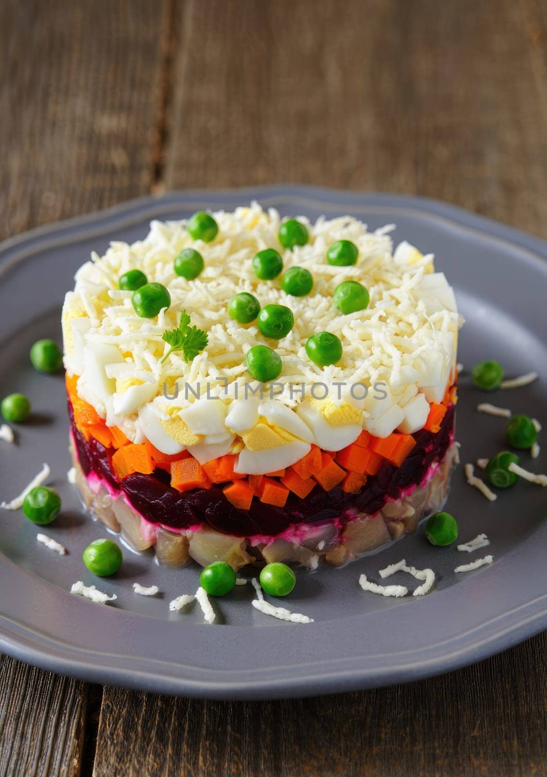 A vibrant layered salad showcasing bright elements like carrots, beets, and eggs, garnished with fresh peas, served on a gray plate. Perfect for festive occasions or gatherings.
