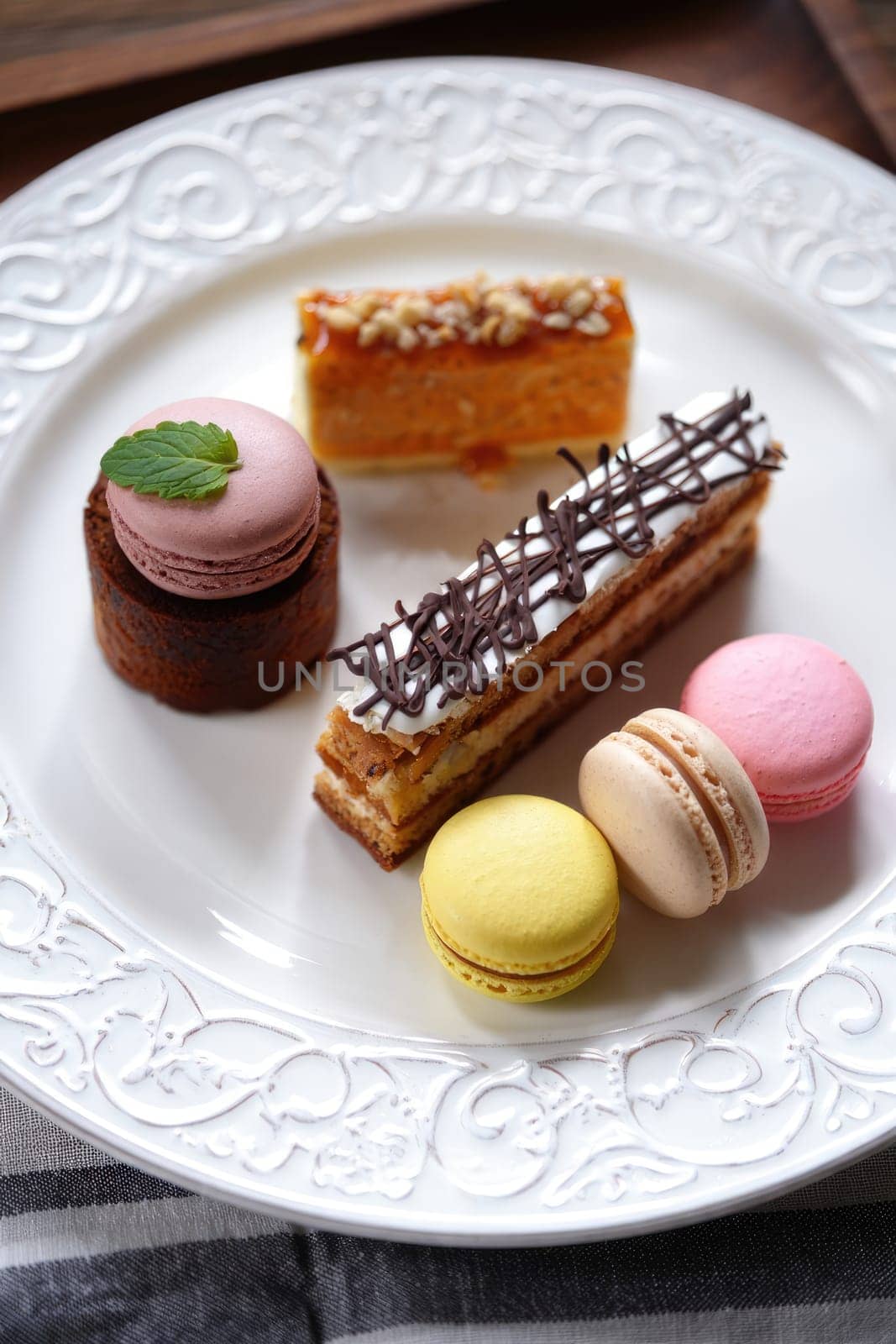 A beautifully arranged plate features an array of pastries including layered cakes and colorful macarons. The desserts showcase a variety of textures and flavors, perfect for a sweet afternoon treat.